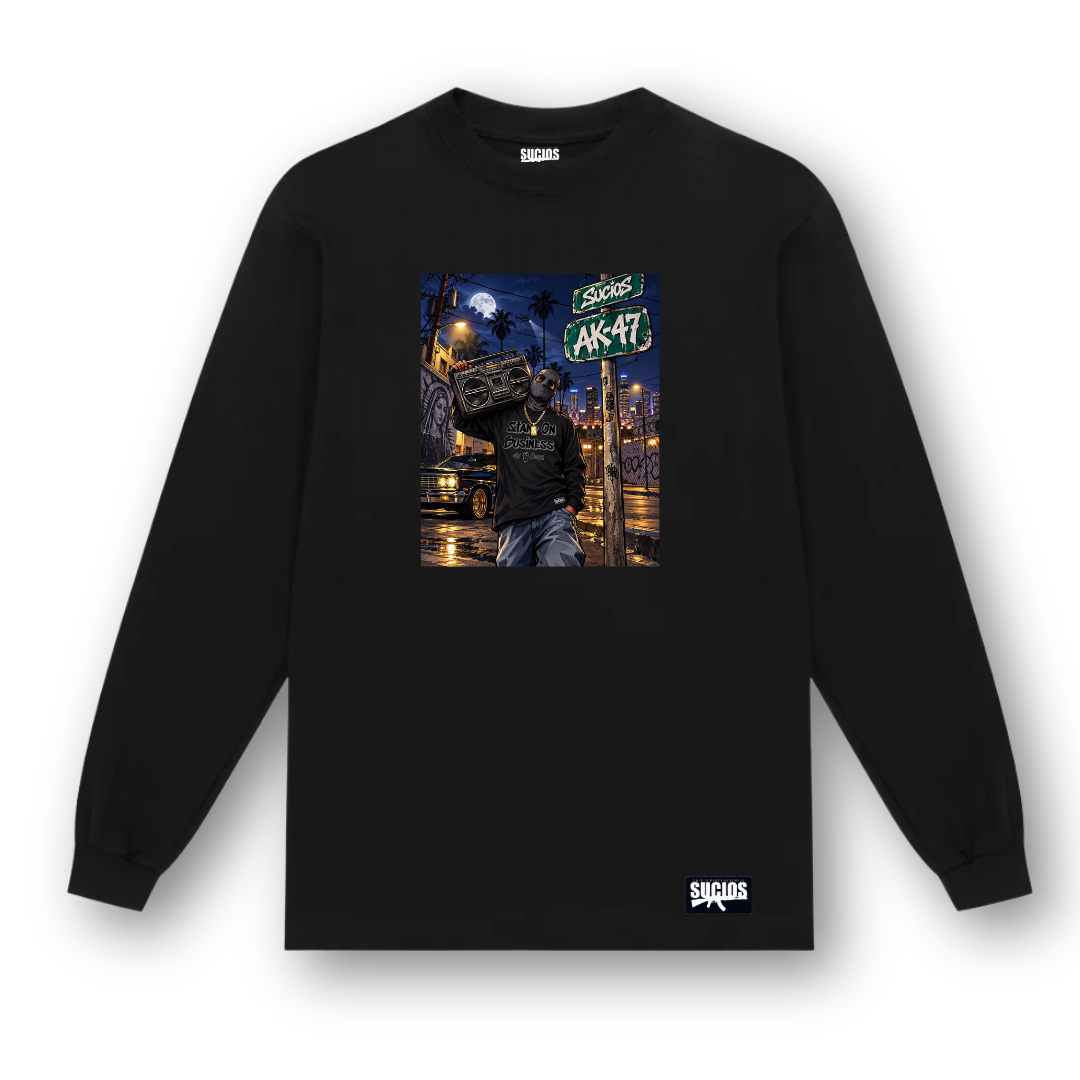 A black long-sleeve crewneck sweatshirt with a colorful graphic print on the chest depicting a street scene with a boombox and the text 'SUCIOS AK-47'. A small white 'SUCIOS' brand logo is printed on the bottom right hem.