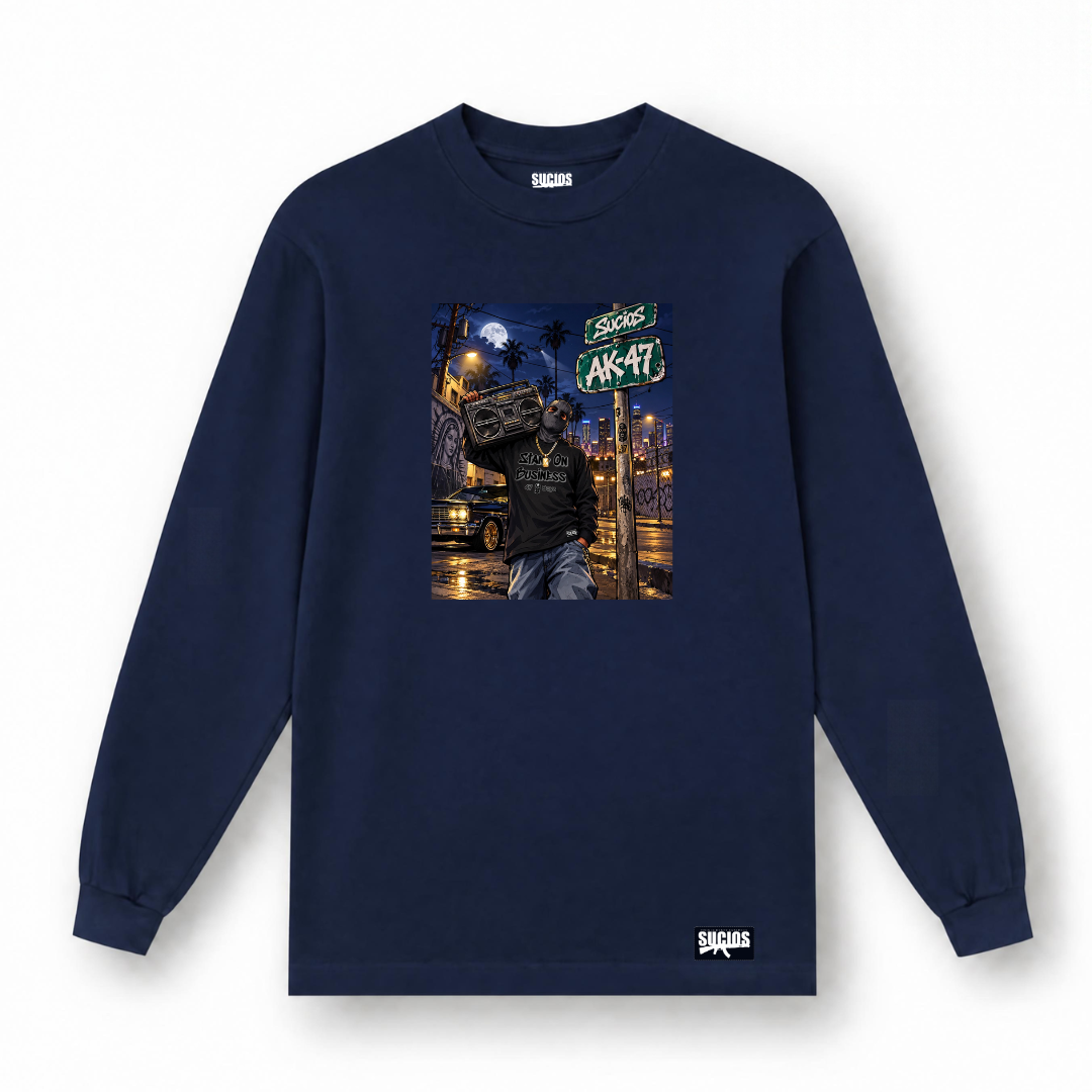 A navy blue long-sleeve t-shirt with a central graphic print of a person carrying a boombox on a city street at night, featuring a 'SUCIOS AK-47' sign. The brand name 'SUCIOS' is visible on the inner neck label and printed in white near the bottom hem.
